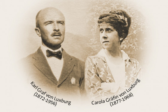 Portraits von Graf Karl und Gräfin Carola. Der Graf schaut nach rechts. Er trägt einen Schnurrart und ein Jackett mit Fliege. Die Gräfin schaut nach links. Ihre Haare sind hochgesteckt und sie trägt ein Kleid. Unter den Portraits steht: Karl Graf von Luxburg (1872-1956) und Carola Gräfin von Luxburg (1877-1968).