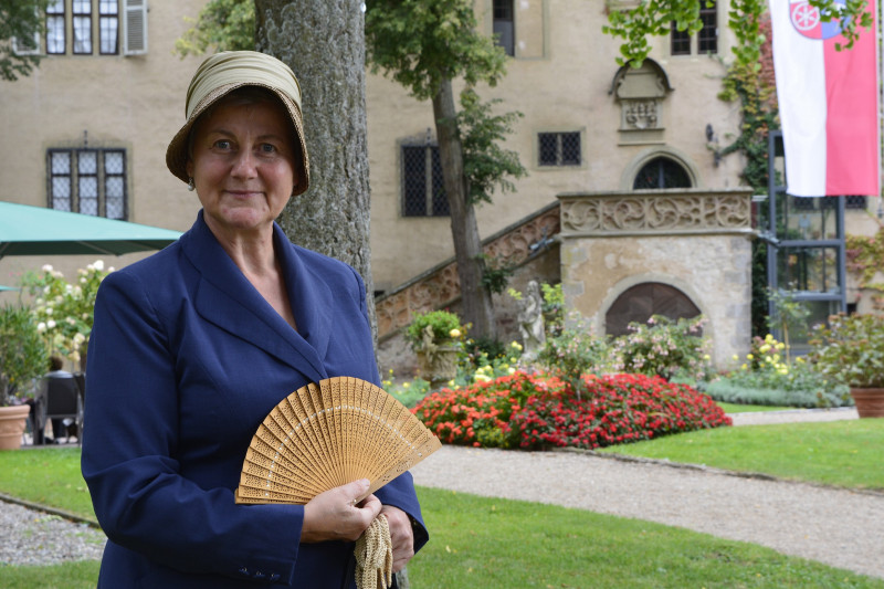 Eine Museumspädagogin hat sich als Gräfin Carola verkleidet. Im Hintergrund befindet sich das Schloss.